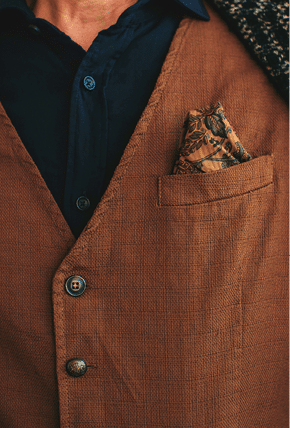 Closeup of crop incognito man wearing woolen checkered brown blazer with dark blue shirt and brown vest with flower pocket square