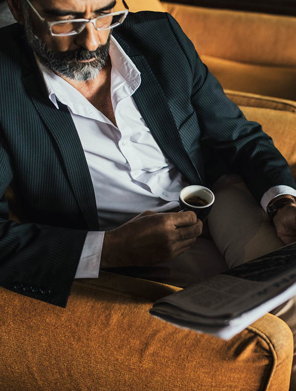 Elegant Caucasian businessman drinking coffee and reading newspaper 