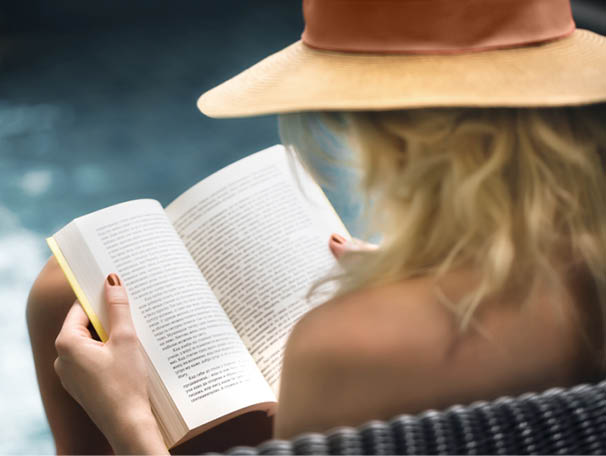 Caucasian woman sitting by a swimming pool and reading a book 