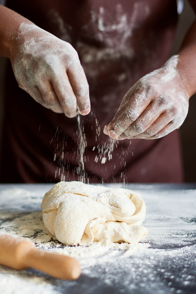 Close-up view of unrecognizable African American cook in apron sprinkling dough with flour while making homemade bread